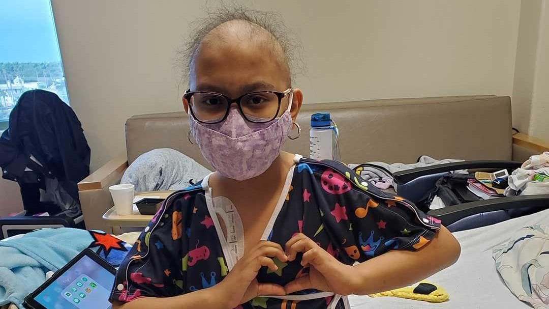 Hospitalized child wearing a Starlight Hospital Gown while holding hands up in a heart shape.